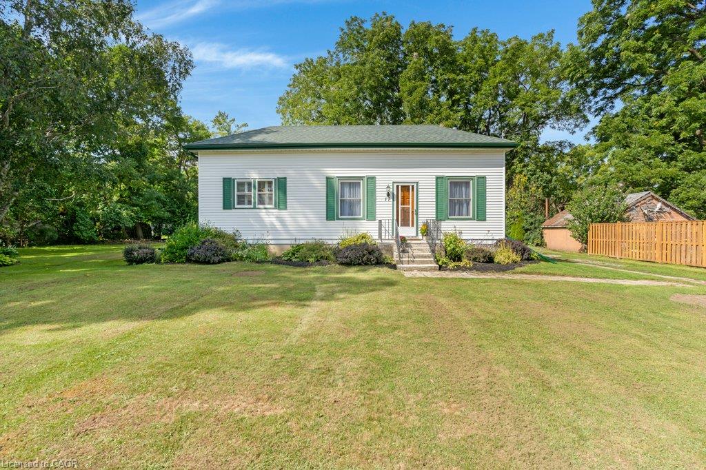 Classic cottage-style home featuring a clean white exterior with green shutters, a welcoming front entrance with steps and a covered porch, and mature landscaping with flowering shrubs