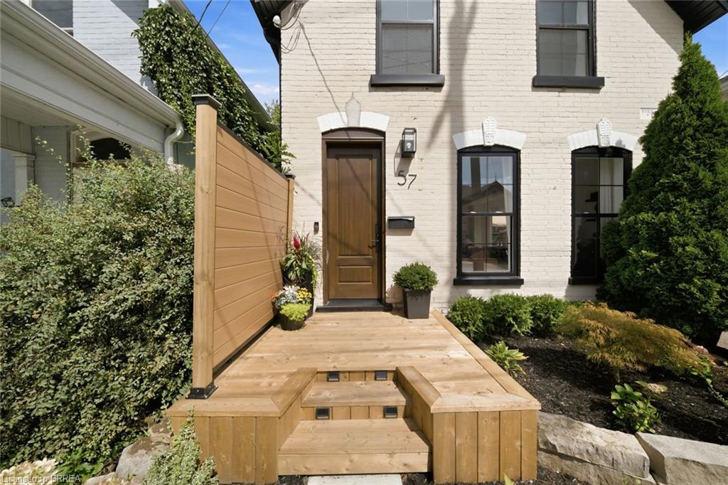 White brick exterior, wooden privacy screen, multi-level wooden deck, black framed windows, dark wood entry door