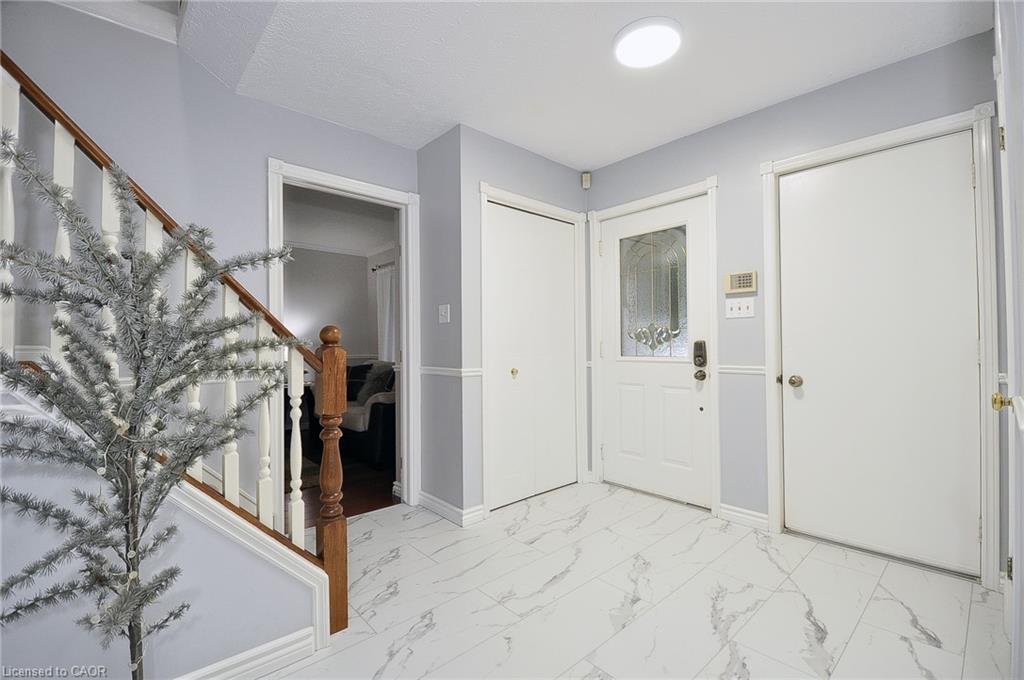 White-finish front door with decorative glass inserts, white-finish doors, wood-finish stair railing with white balusters, and white-finish flooring with gray veining