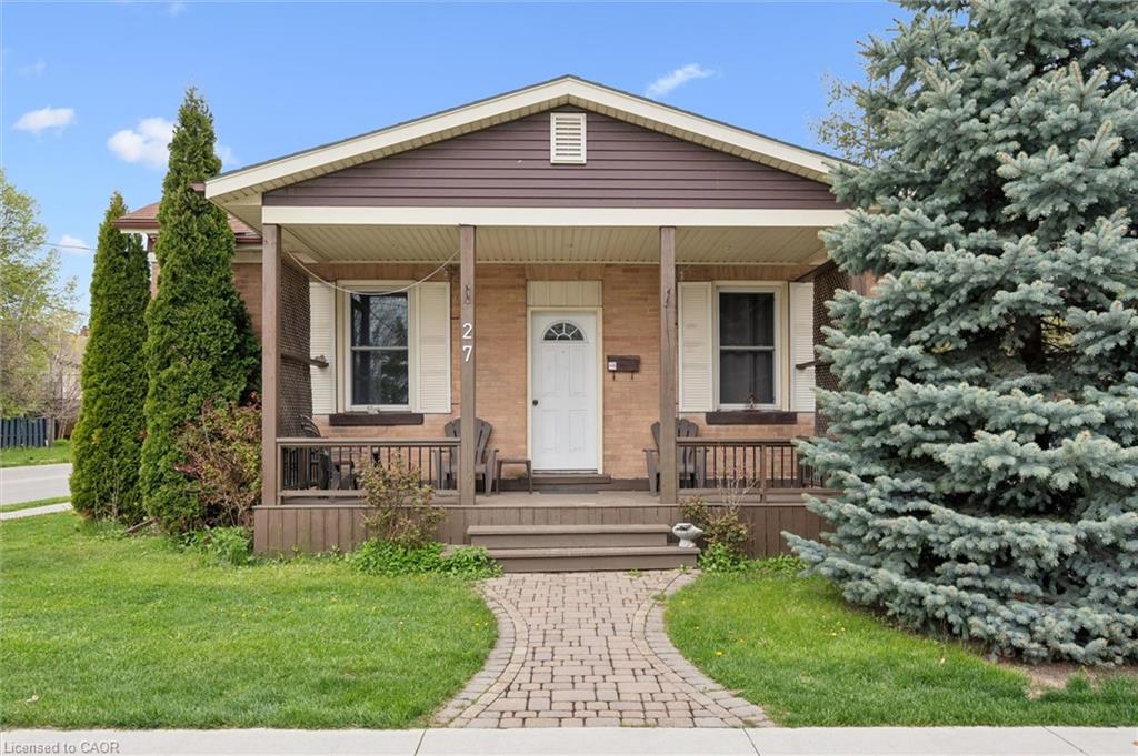 Brick facade with brown siding, covered front porch with wood columns and railing, front yard with mature landscaping, and a paver stone walkway