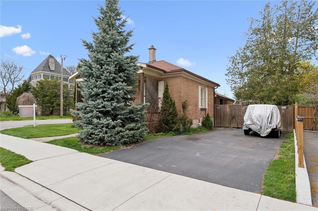 Brick exterior with a brown shingle roof, paved driveway, mature conifer, and wood fencing