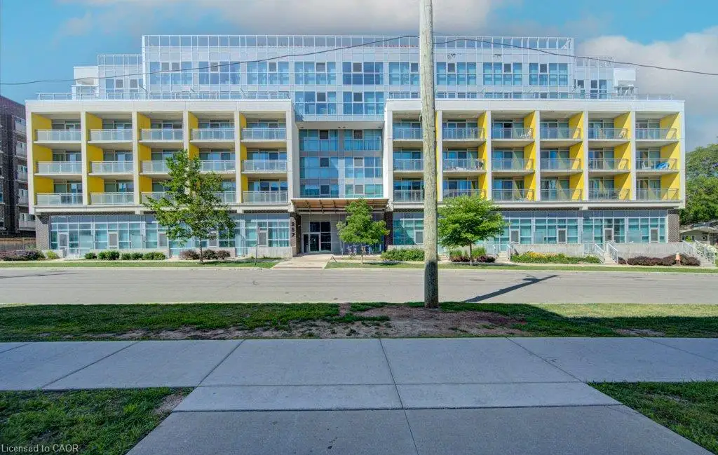 Contemporary multi-story building featuring a glass facade, yellow balcony accents, ground-level commercial spaces, and integrated street-level landscaping