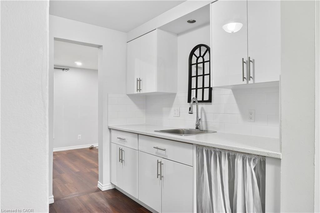 White shaker-style cabinetry with chrome hardware, subway tile backsplash, stainless steel sink with a gooseneck faucet, and light-toned countertop