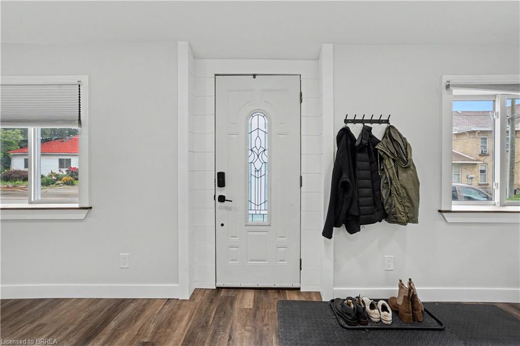 Wood-finish flooring, white walls, white trim, two windows with blinds, and an entry door with decorative glass