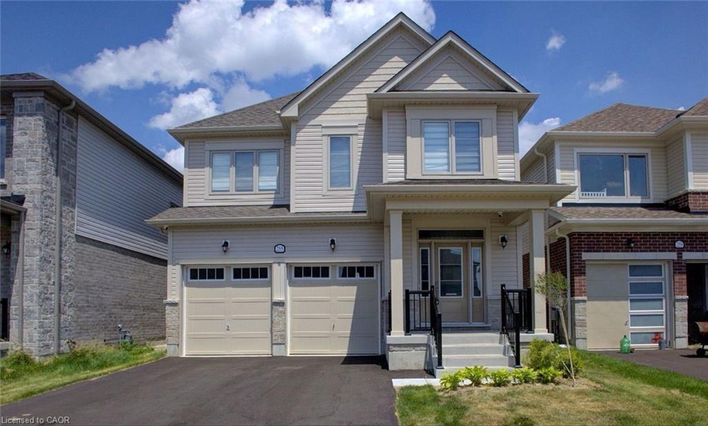The property features a two-car garage with a paved driveway, a covered front porch with steps and railings, and an exterior constructed with light-colored siding and stone accents