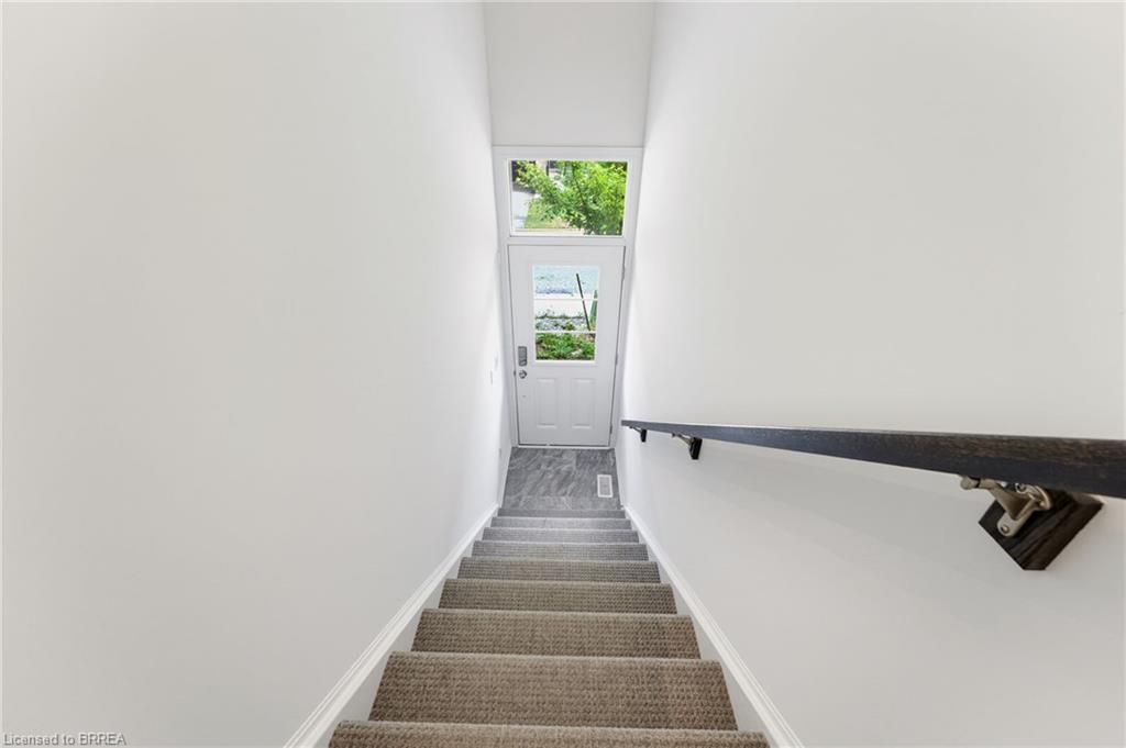Carpeted staircase with a dark wood-finish handrail leading to an exterior door with transom window and a tiled landing