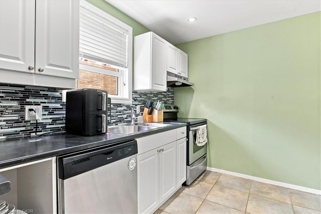 White cabinetry with brushed nickel hardware, dark countertops, a mosaic tile backsplash, stainless steel dishwasher, and a stainless steel range with overhead ventilation