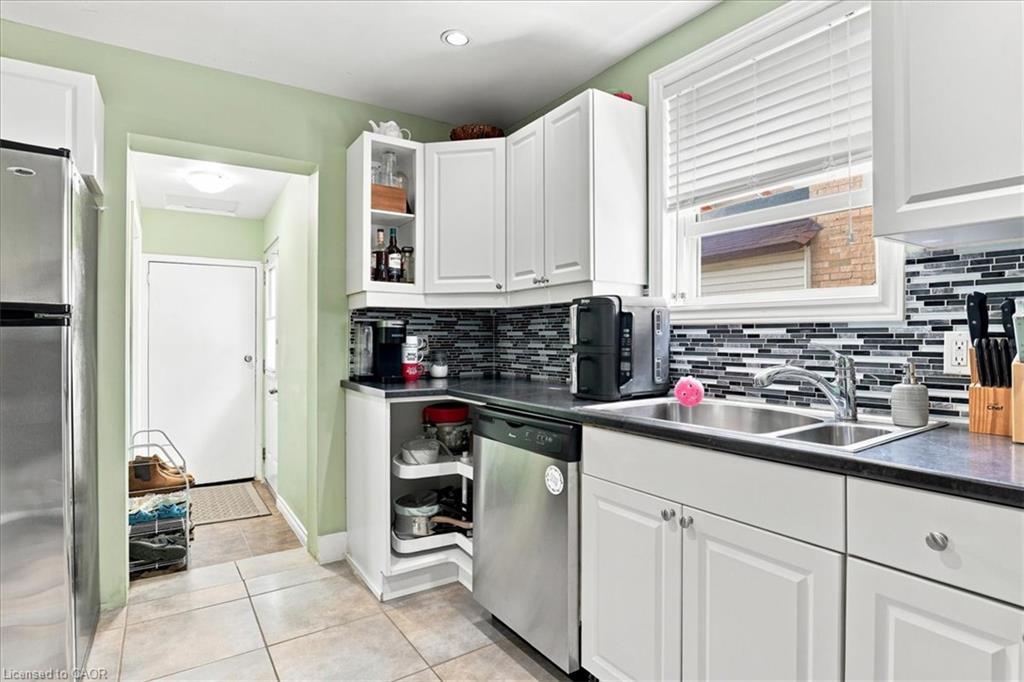 Stainless steel dishwasher, dual basin sink with chrome faucet, black countertops, white cabinetry with silver hardware, and a mosaic tile backsplash
