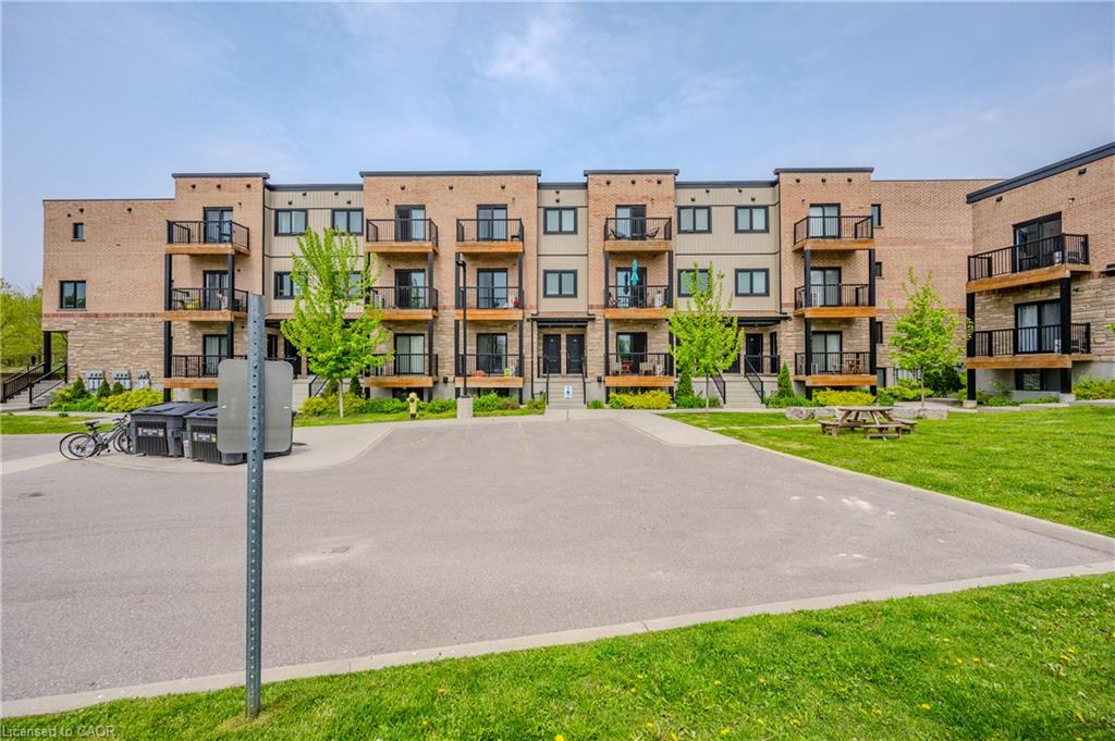 Multi-story building featuring brick and stone cladding, multiple private balconies with black railings, and an expansive paved parking area