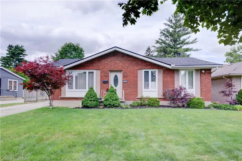 Brick facade residence featuring a front lawn, mature landscaping, a paved driveway, and a shingled roof