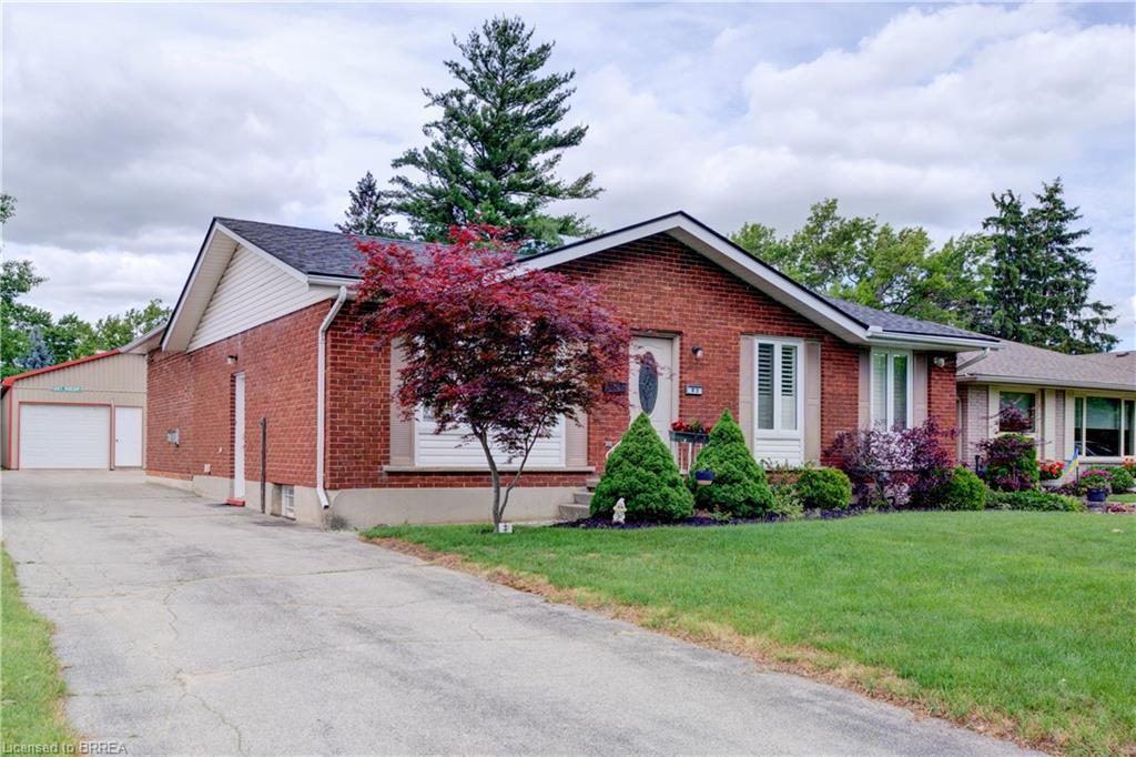 Brick exterior residence with a gabled roofline, featuring a paved driveway, an attached garage, and a detached auxiliary structure with a garage door