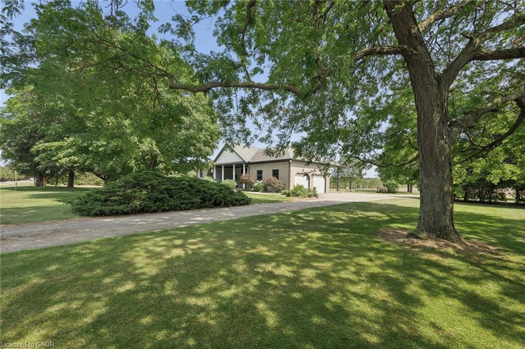 Expansive front yard featuring mature shade trees, a manicured lawn, and a gravel driveway