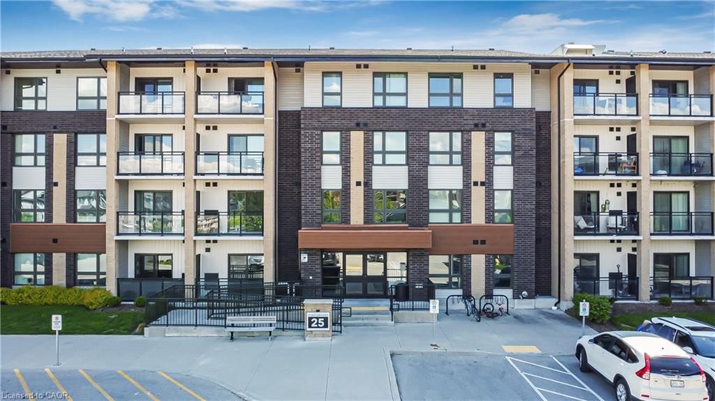 Modern multi-story building featuring a brick and stucco facade, multiple private balconies with glass railings, a prominent main entrance, and a paved parking area