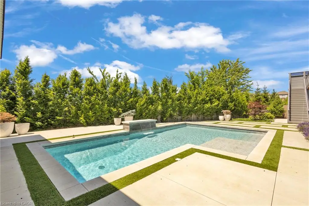 In-ground swimming pool featuring a water feature, stone coping, concrete decking, and artificial turf borders