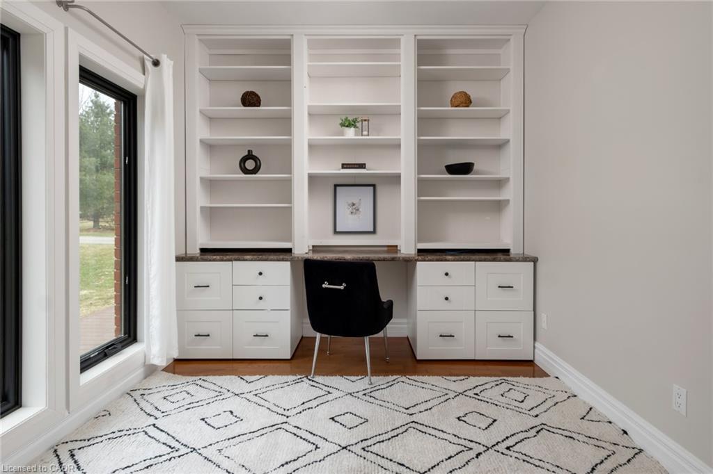Built-in white shelving, integrated desk, lower cabinetry with black hardware, wood-finish flooring, and bright window