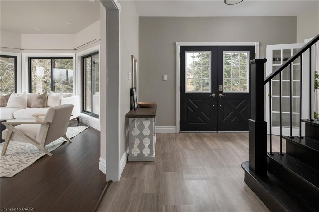 Welcoming foyer featuring dark wood-finish flooring, black dual barn doors with glass panes, metal stair railing, and abundant natural light from transom windows