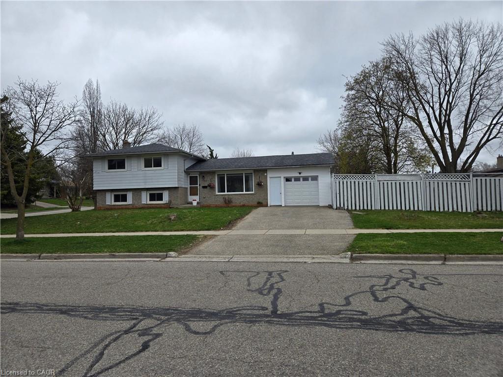 Split-level residence featuring a brick and siding exterior, an attached single-car garage, a concrete driveway, a manicured lawn, and a white picket fence