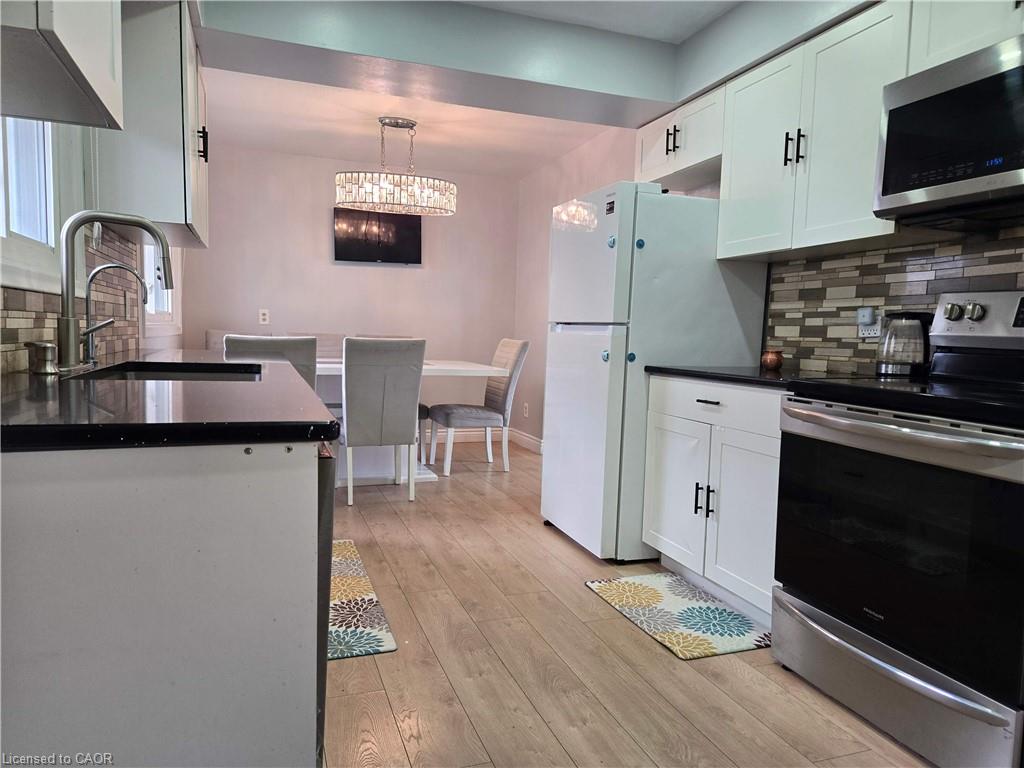 Kitchen featuring light wood-finish flooring, white cabinetry with black hardware, dark countertops, and a mosaic tile backsplash