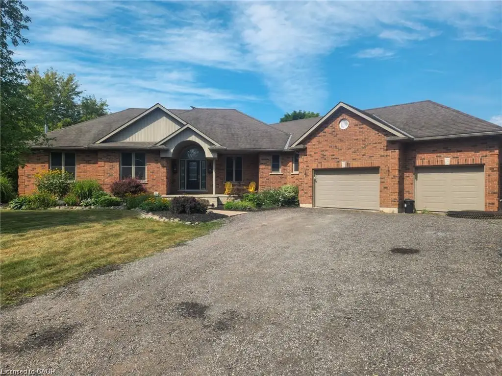 Brick exterior with a prominent arched entry, dual garage doors, gravel driveway, and landscaped front garden beds