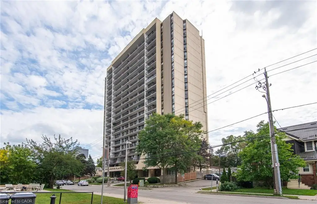 High-rise building with multiple levels of private balconies, a paved parking area, and mature trees