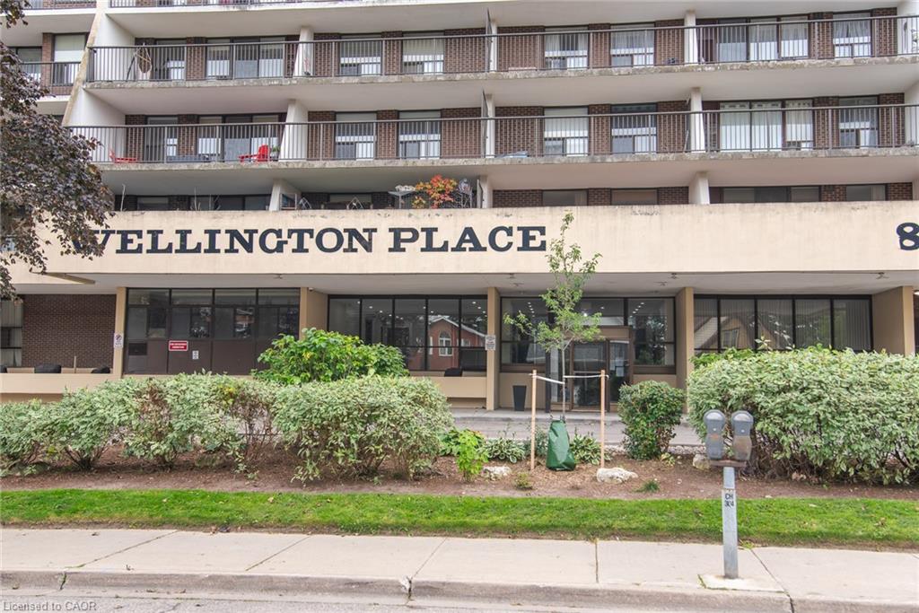 Building exterior featuring a prominent "WELLINGTON PLACE" sign, ground-level windows, and multiple balconies with dark railings