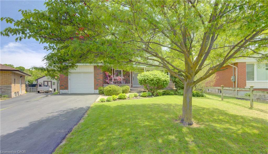 Brick exterior home featuring a front porch, an attached single-car garage, a paved driveway, and a mature tree on a manicured lawn