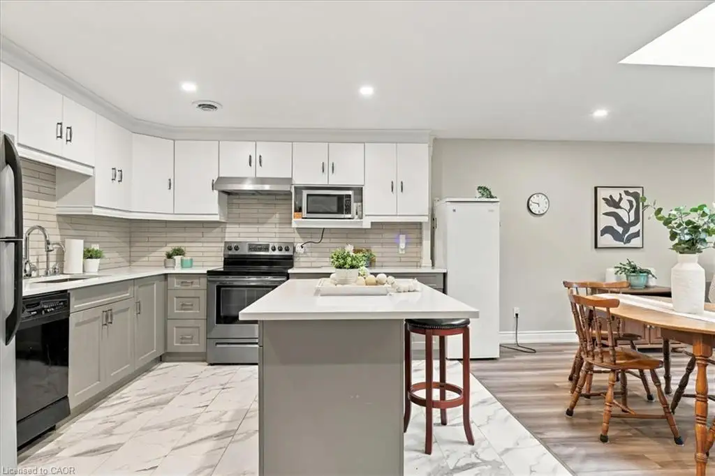 Kitchen featuring two-tone cabinetry, a central island with a solid-surface countertop, stone-pattern tile flooring, and a linear tile backsplash