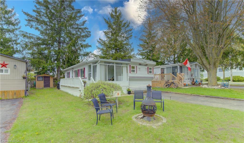 Exterior mobile home featuring white siding with red shutters, an enclosed sunroom, a covered front porch, and a dedicated storage shed