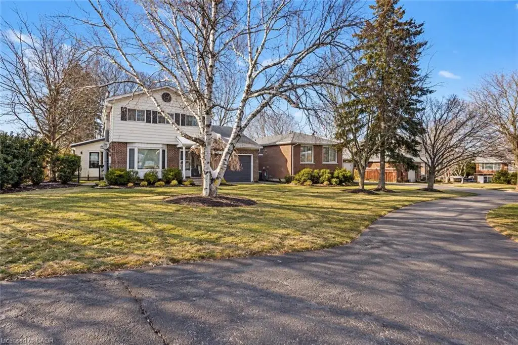 Two-story residence featuring a brick and siding exterior, bay window, attached garage, and paved driveway situated on a lot with mature trees