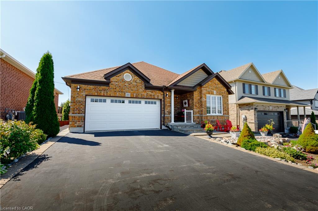 Brick Colonial home featuring a two-car attached garage with white panel doors, circular window detail above the entry, and manicured landscaping with mature evergreen plantings and seasonal flower beds flanking the driveway