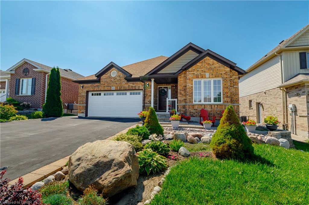 Charming brick and stone ranch featuring a two-car garage, manicured front landscape with mature evergreen plantings and natural stone accents, and a welcoming entry with architectural detailing