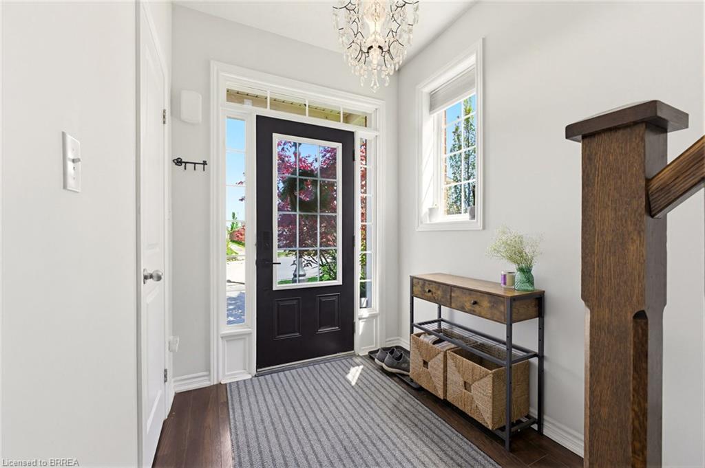 Rich wood-finish flooring, a black front entry door with sidelights, and a crystal chandelier