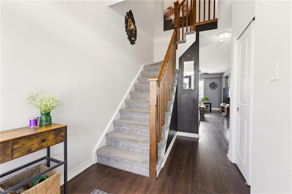 Wood-finish flooring, staircase with carpeted treads, wood banister and spindles, and a white interior door