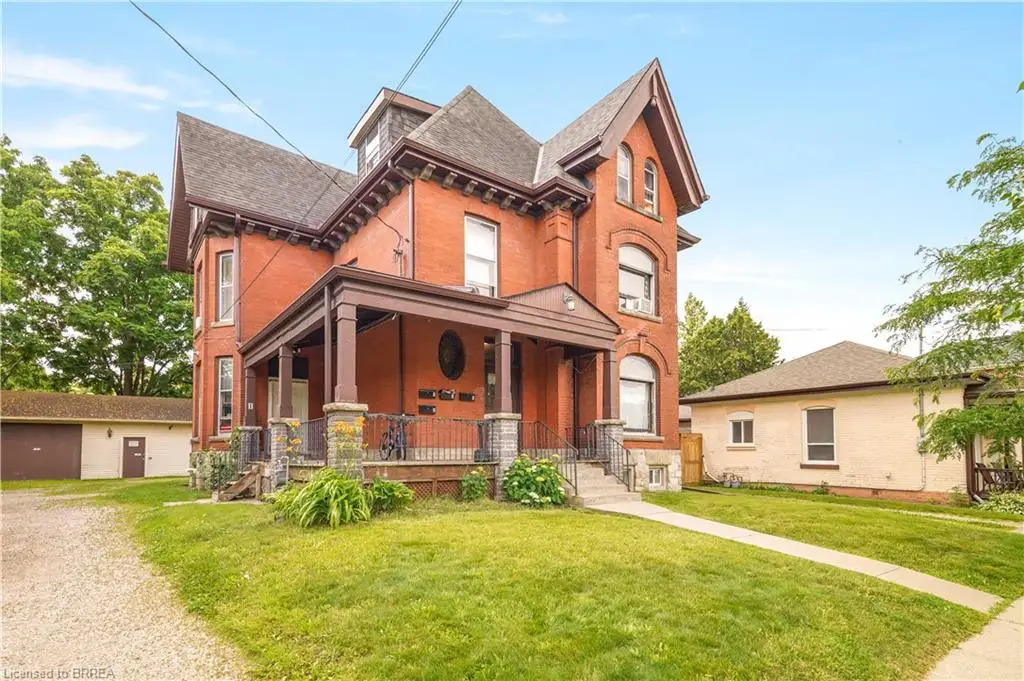 Multi-story brick structure featuring an expansive covered front porch with stone pillars