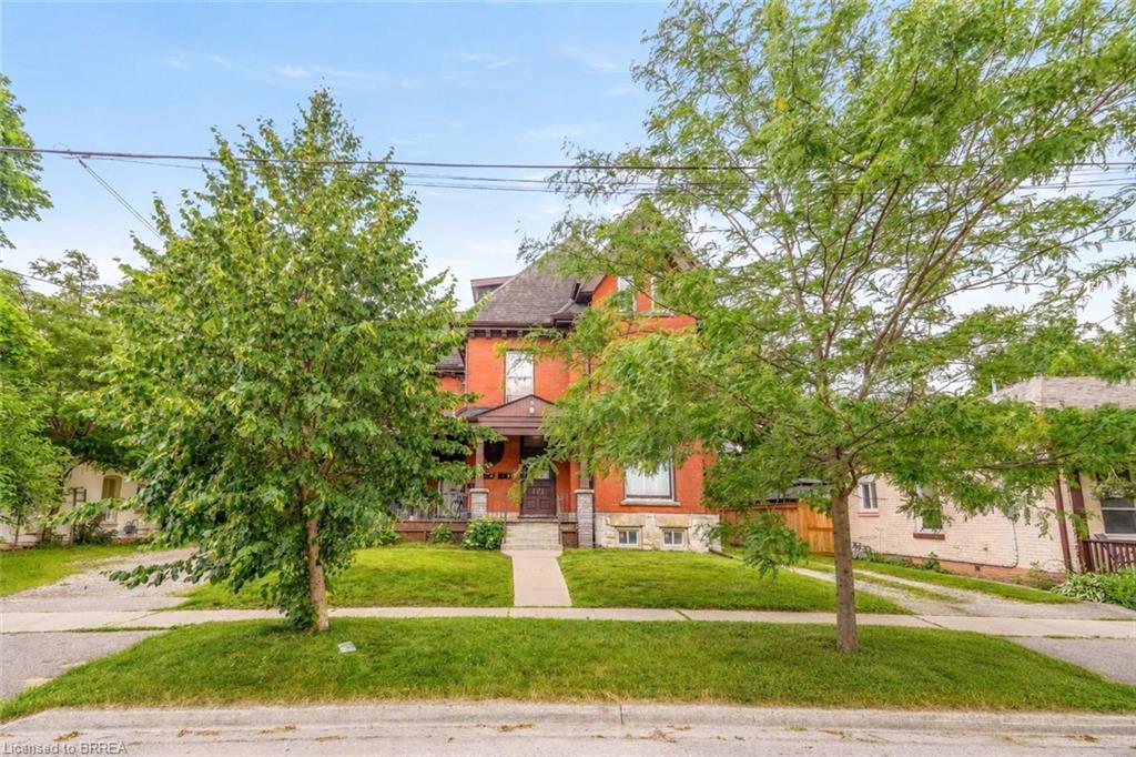 Brick residence featuring a covered front porch, gabled roofline, and mature front yard trees