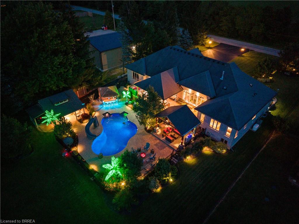 Expansive backyard oasis featuring a freeform swimming pool, multiple covered patio areas, dedicated pool house, and extensive paved hardscaping