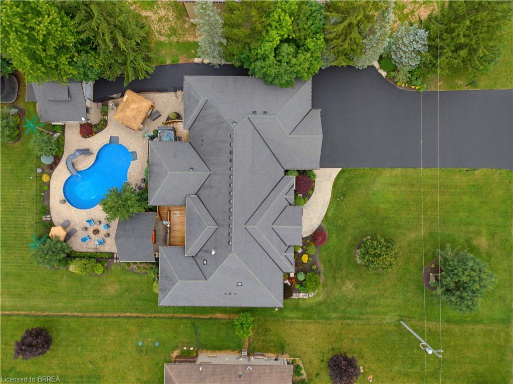 Expansive property featuring a dark-colored multi-gabled roof, a large custom-shaped swimming pool with a slide, a paved patio surround, a dedicated fire pit area, and a dark-paved driveway