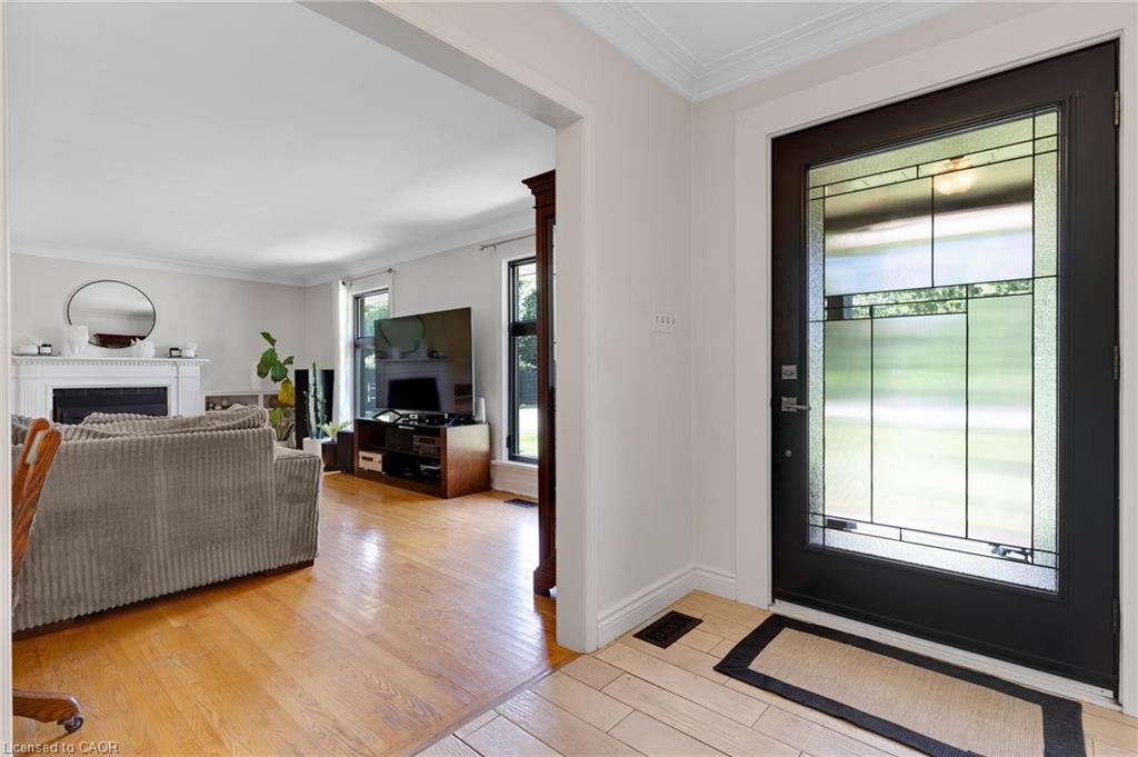 Entry door with decorative glass panels, crown molding, wood-finish flooring, white fireplace with mantel, and recessed lighting