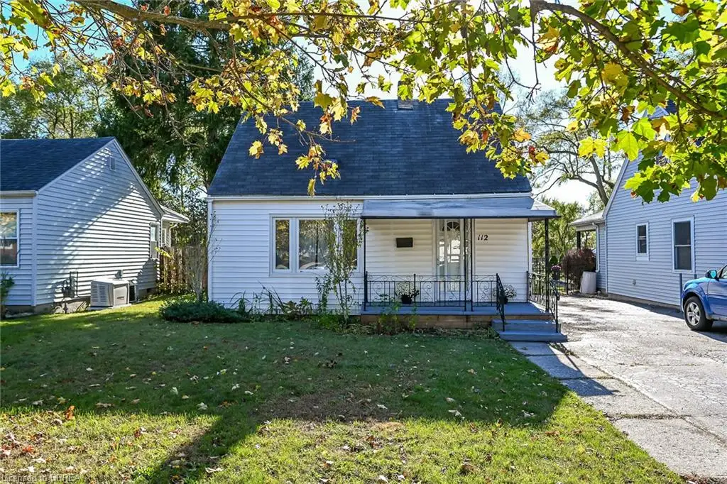 Exterior facade featuring white siding, a covered front porch with iron railings, a gabled roofline, and a paved concrete driveway