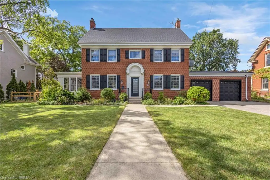 Brick exterior with black shutters, two-car garage, manicured lawn, and concrete pathway