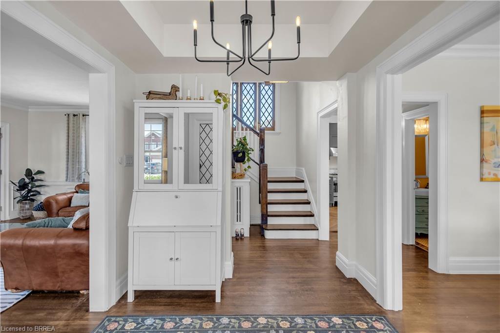 Hardwood flooring, white trim, recessed ceiling with a contemporary chandelier, and a wood staircase with white risers