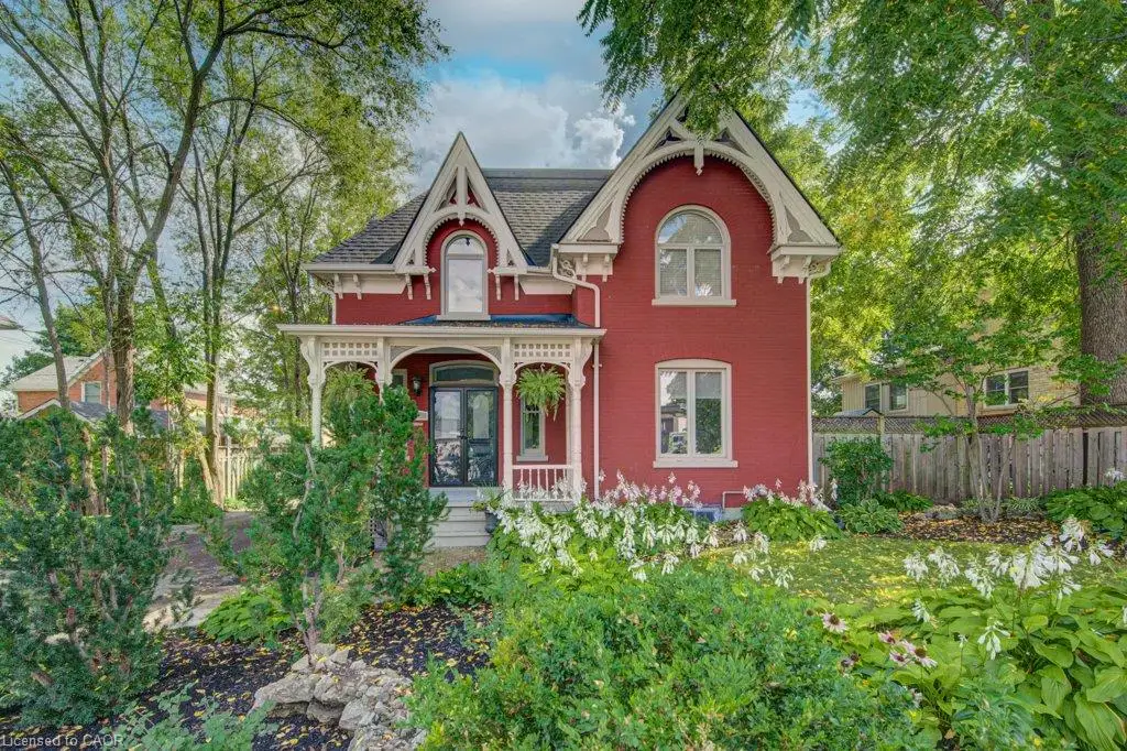 Victorian architecture featuring a red exterior, decorative white trim, a covered front porch, and mature landscaping