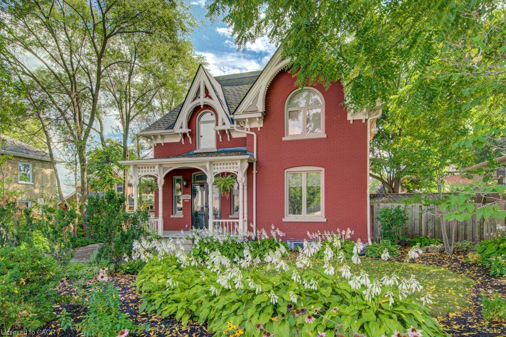 Red brick exterior with white trim and decorative gable detailing, featuring an arched window and a covered front porch with ornate railings