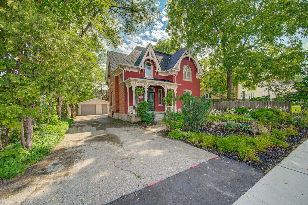 Red brick exterior with white trim, covered porch with decorative railing, arched windows, landscaped front yard, and a detached two-car garage