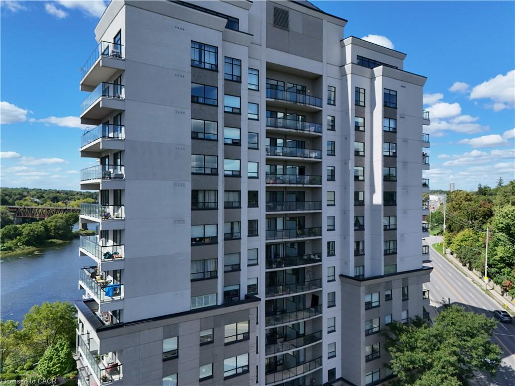Modern multi-story building featuring extensive glazing, private balconies with glass railings, a grey and white façade, and a prominent river backdrop