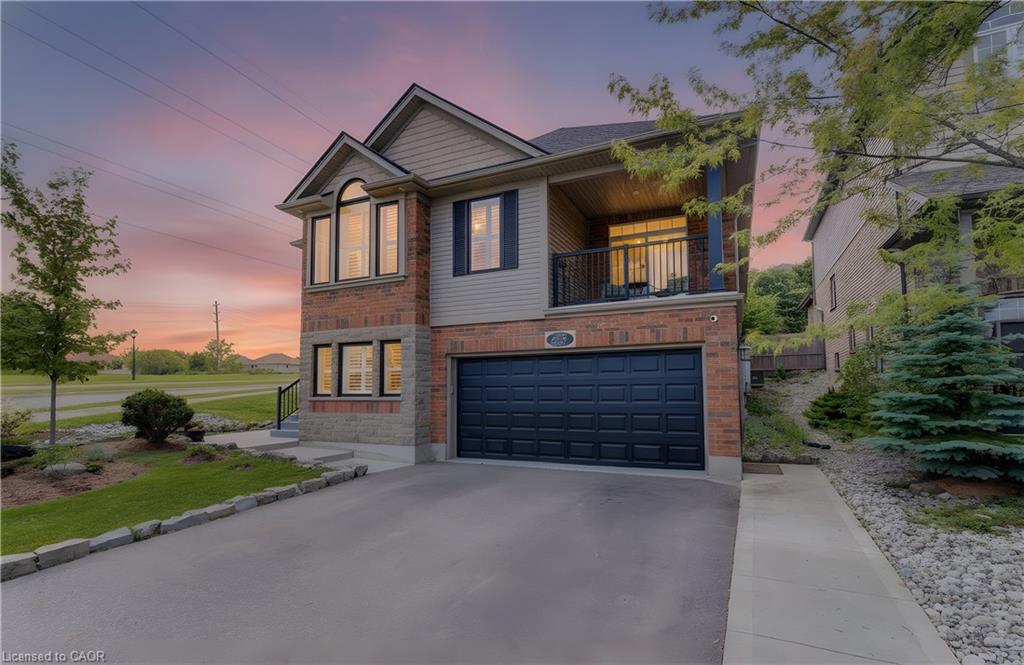Two-story residence featuring brick and siding exterior, an integrated garage with a dark panel door, an upper-level balcony with black railings, and a paved driveway with stone edging