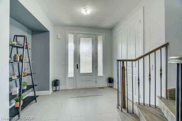 Entryway with light tile flooring, a paneled front door with frosted glass sidelights, and a staircase featuring wood-finish treads and an iron railing