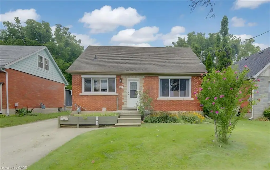 Red brick facade with stone accents, shingled roof, white-framed windows, and manicured front lawn