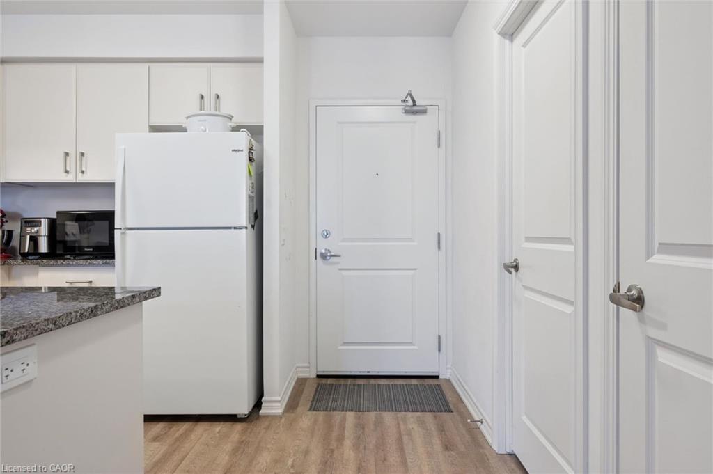 Kitchen featuring freestanding refrigerator, white cabinetry, light wood finished floors, black microwave, and dark stone countertops