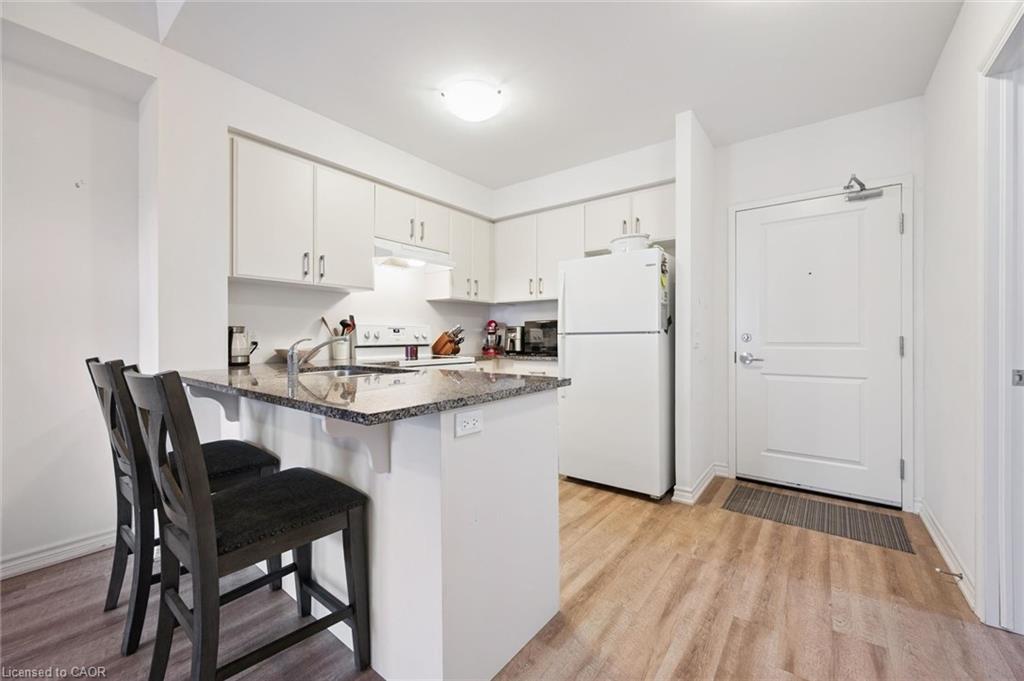 Kitchen featuring a kitchen breakfast bar, white appliances, white cabinetry, a peninsula, and light wood-style floors